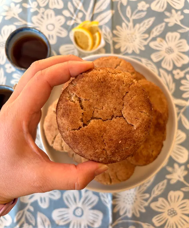 A close-up of a Cinnamon Hug cookie held above a plate of cookies.