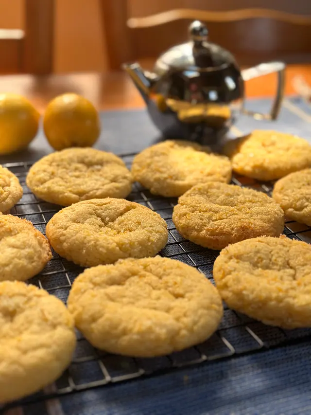 Forever Favourites_Zesty Cookie cookies cooling on a rack with lemons and a teapot in the background.