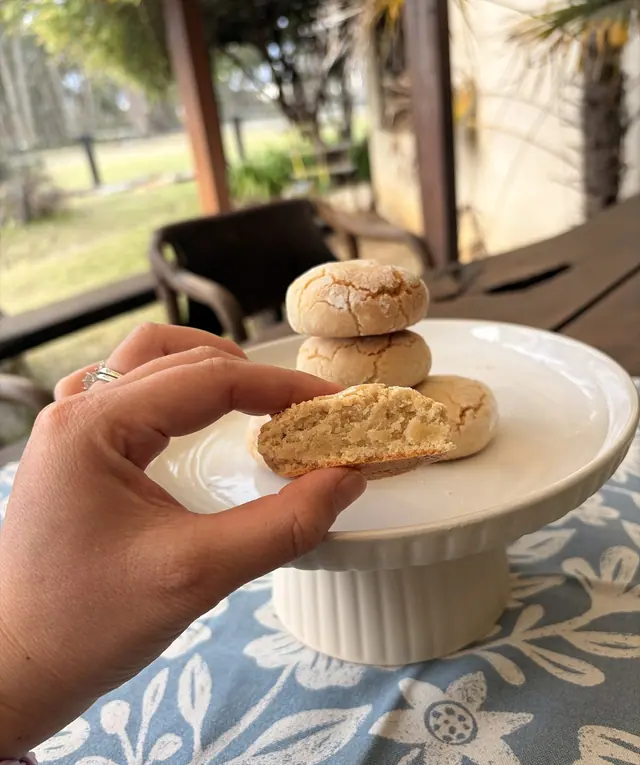 A broken Almond Kiss Italian amaretti cookie shown close-up beside a stack of cookies.
