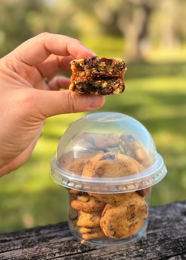 A broken-open chocolate chip Yummy Bite held above a Brownie Points cup outdoors.